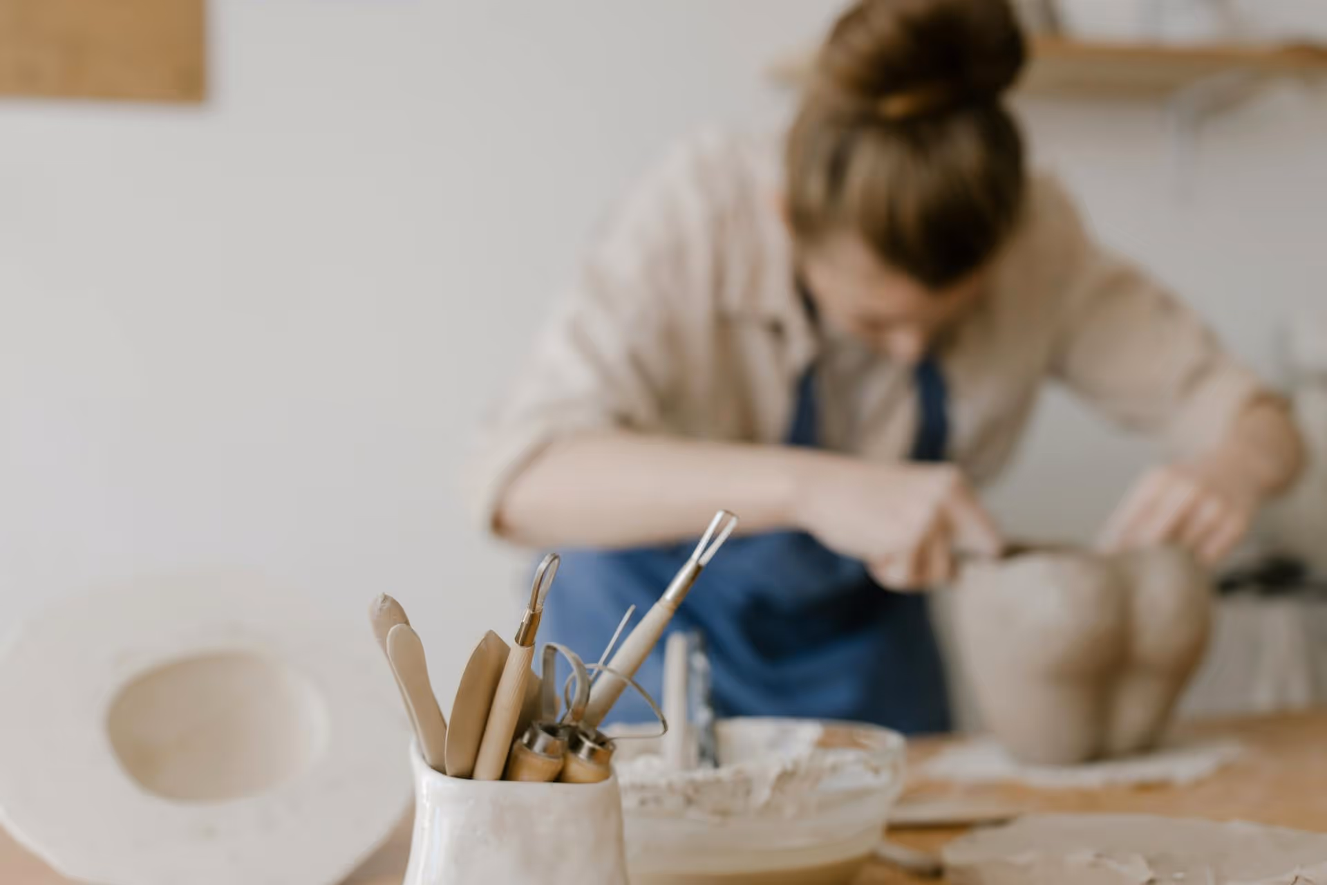Pottery tools in a jar with a person shaping clay in the background.