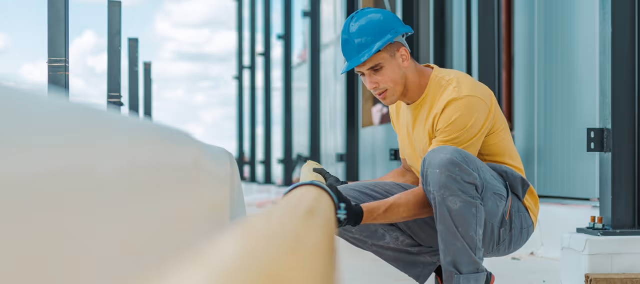 Construction worker wearing a blue hard hat and yellow shirt inspecting a large wooden beam.