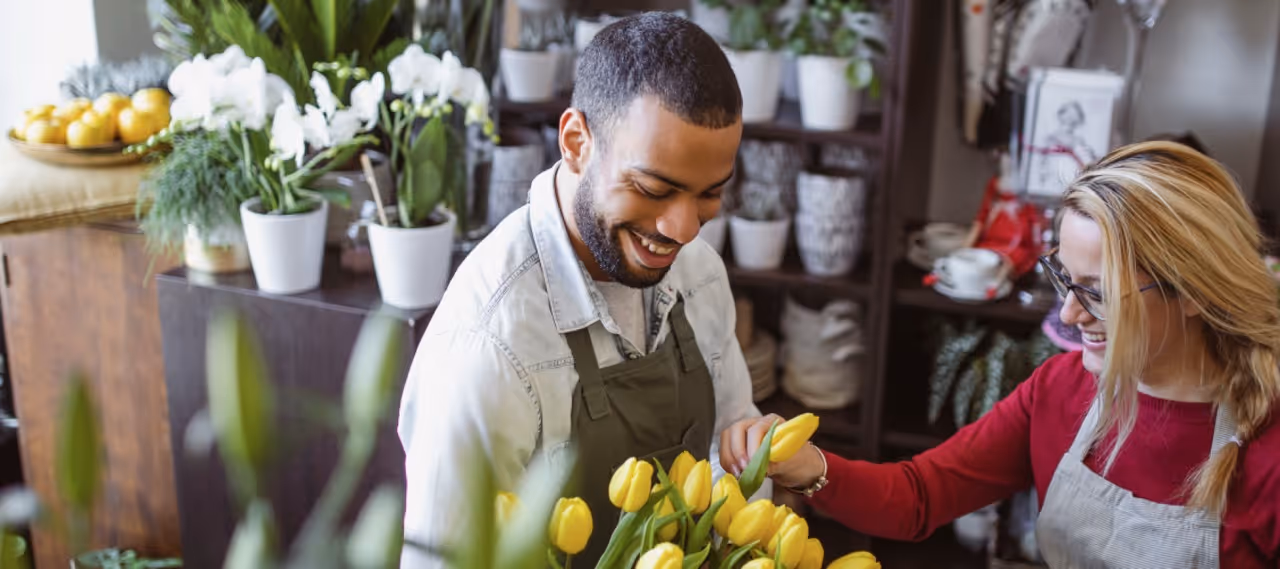 Florists arranging yellow tulips and white orchids in a flower shop with smiles and green plants.