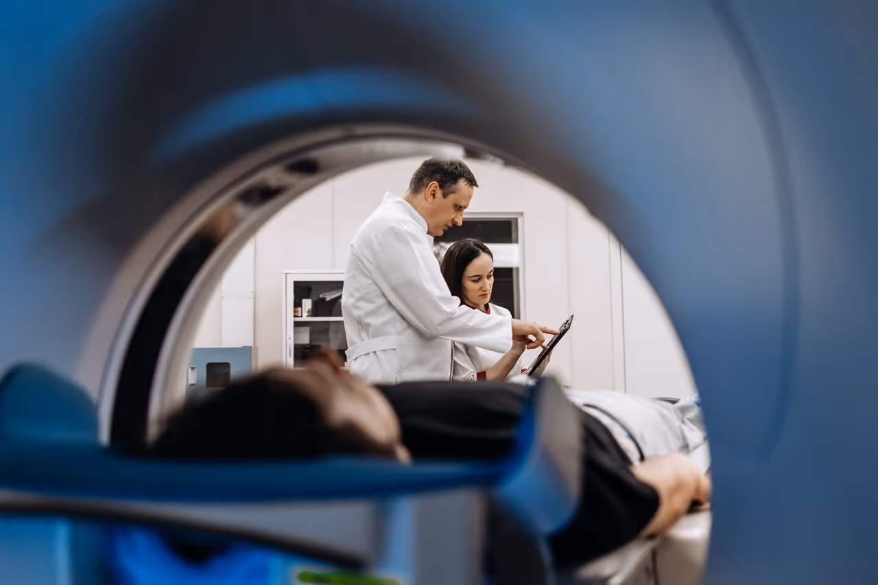 Two doctors in lab coats reviewing a patient's image beside an MRI machine with patient lying inside it.