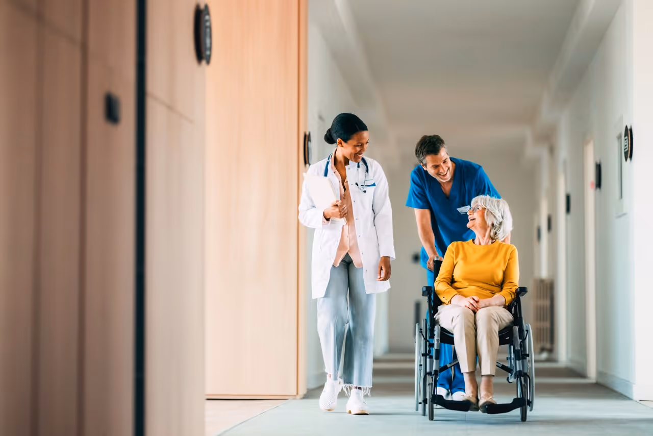 Medical team with doctor and nurse assisting senior woman in wheelchair in hospital hallway.