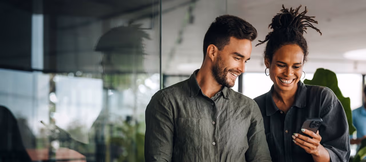 Smiling man and woman looking at a phone together in a modern office space.