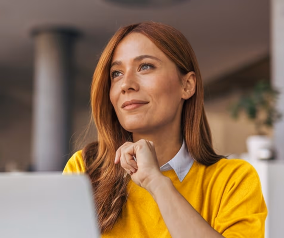 Woman with red hair in a yellow sweater thoughtfully looking away, with a hand near her chin.