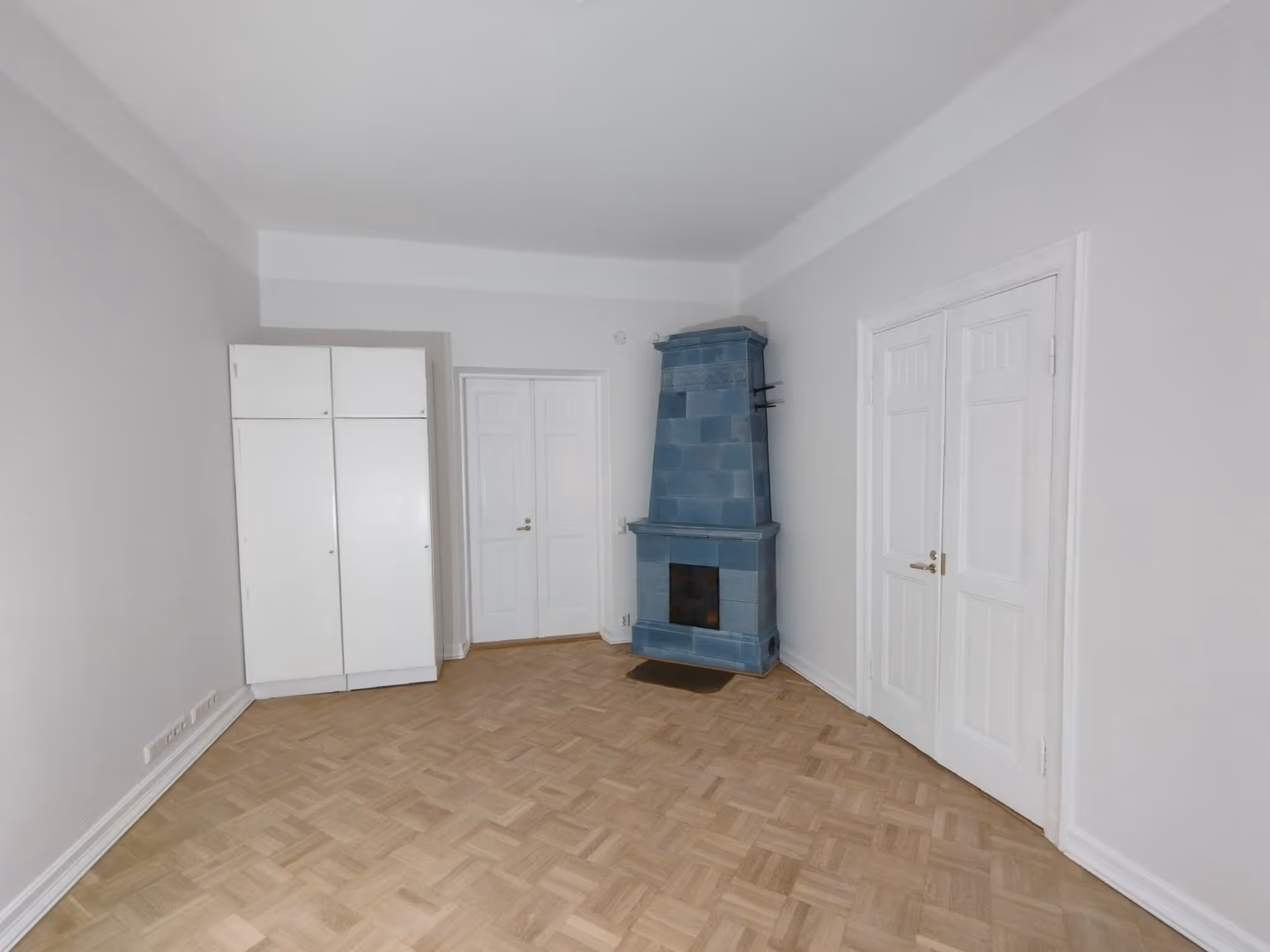 Vaaleassa huoneessa on sininen takka, valkoiset kaapit ja parkettilattia.