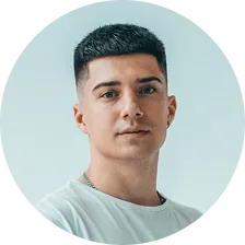 Portrait of a young man with short dark hair and wearing a white shirt against a light background.