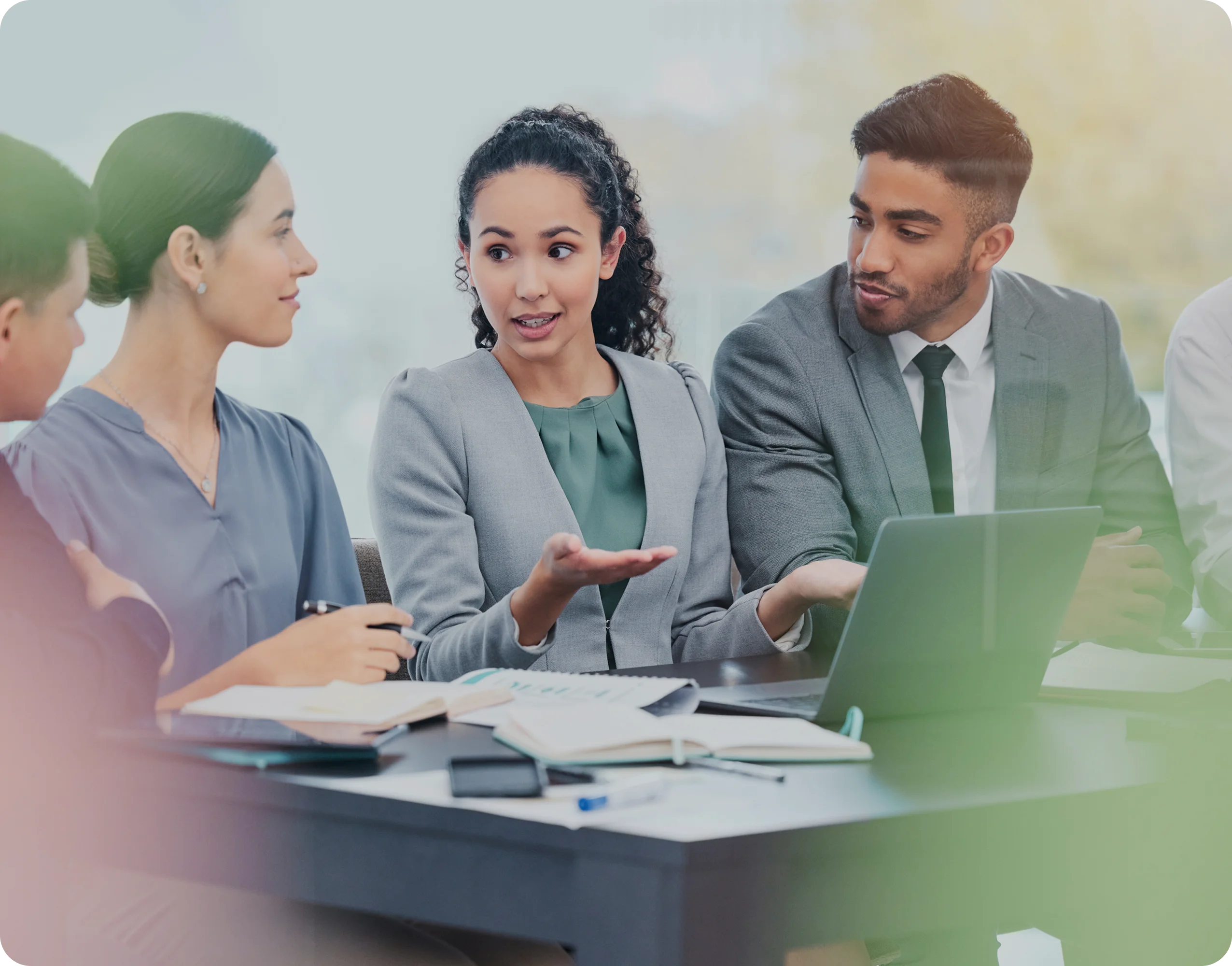 A group of business professionals engaged in a discussion around a table with open notebooks and a laptop.