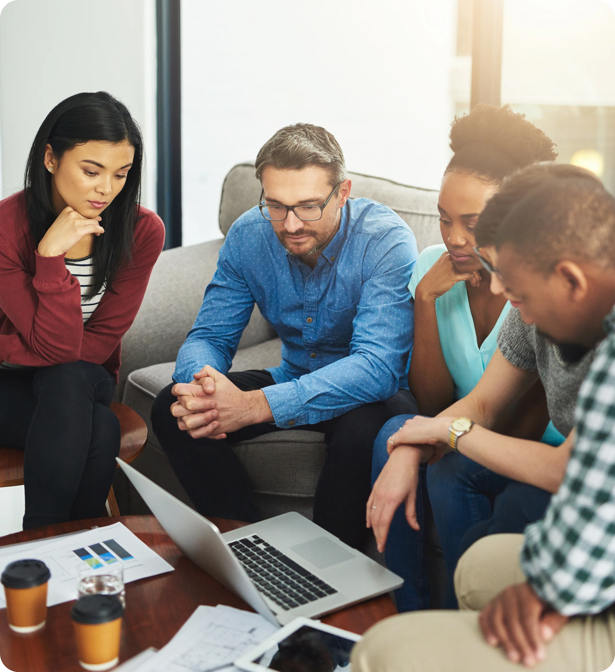 Four diverse colleagues sitting around a table, attentively looking at a laptop screen during a meeting.