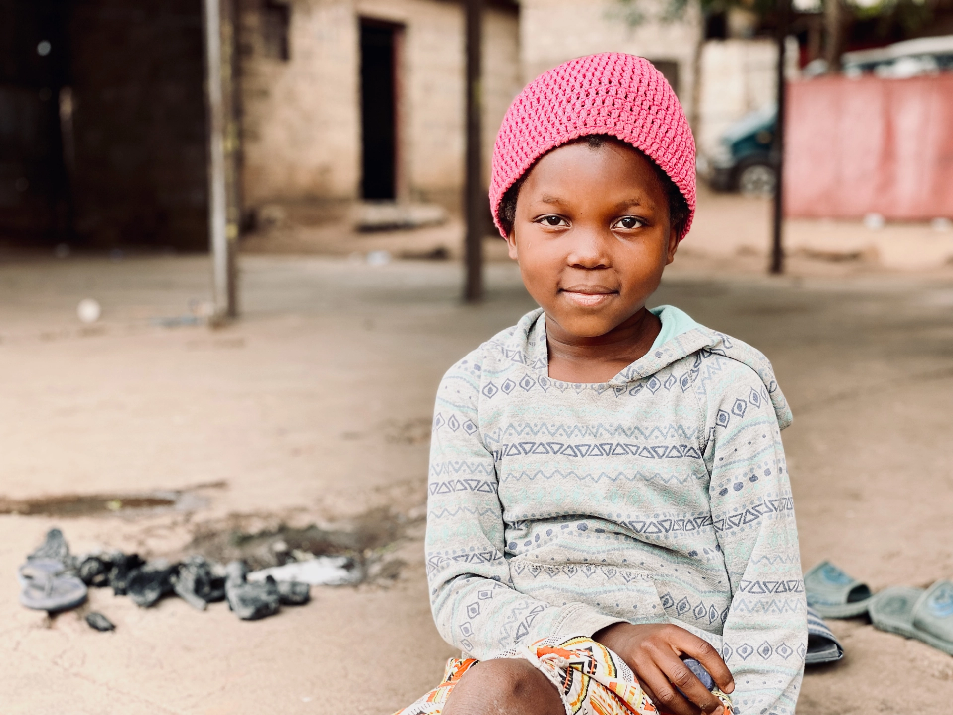 A girl in a pink knitted hat sitting outside her home