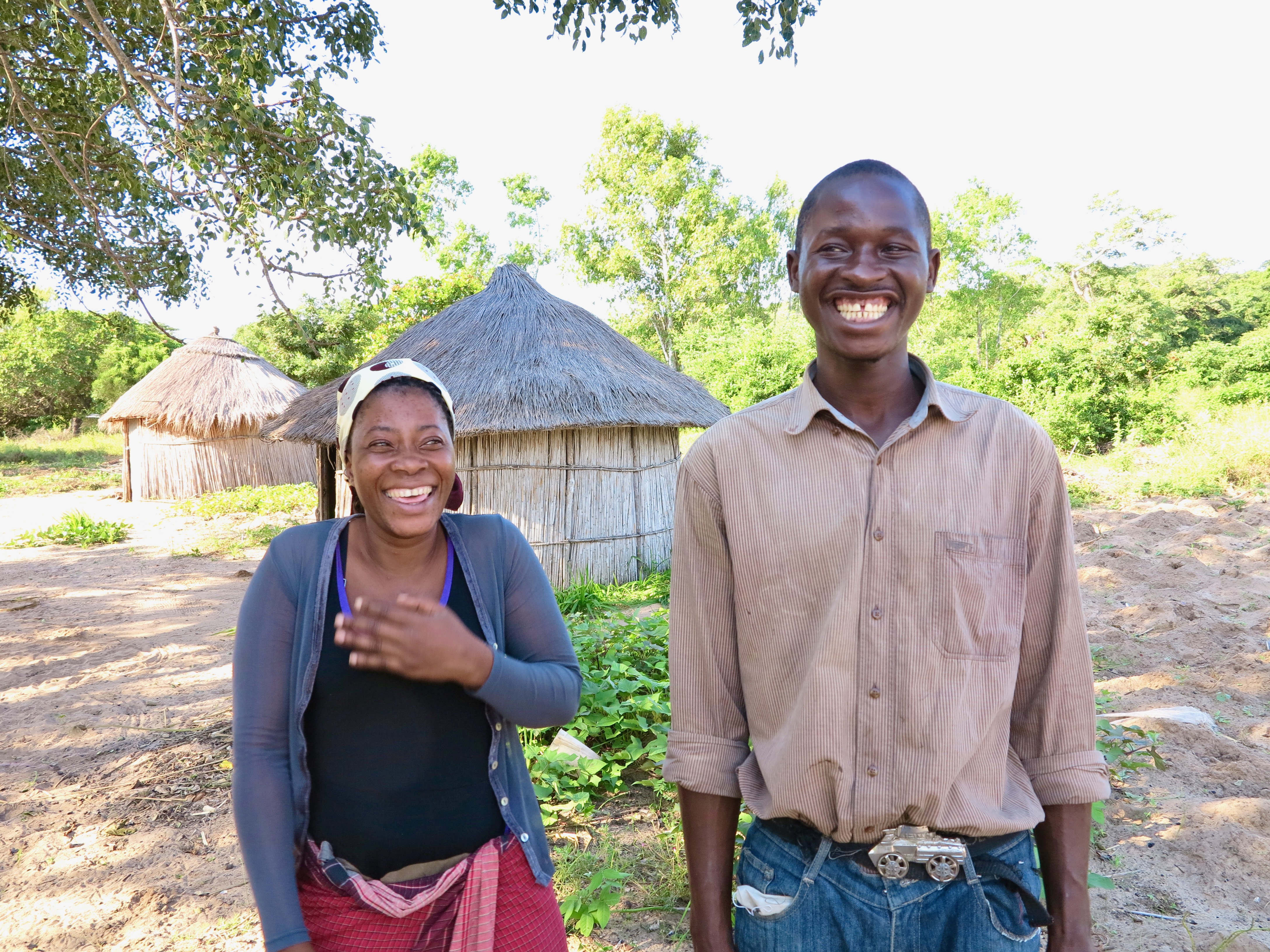 A woman and a man laughing together outside thatched homes