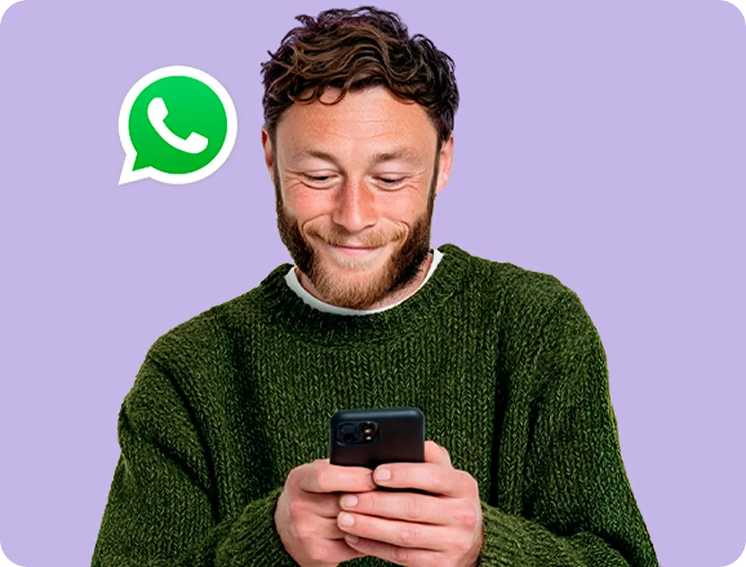 Hombre sonriendo mientras usa un teléfono móvil con el icono de WhatsApp al lado.