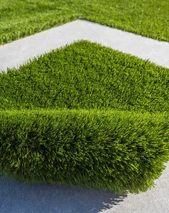 Un rollo de césped artificial verde sobre una superficie gris con un diseño blanco.