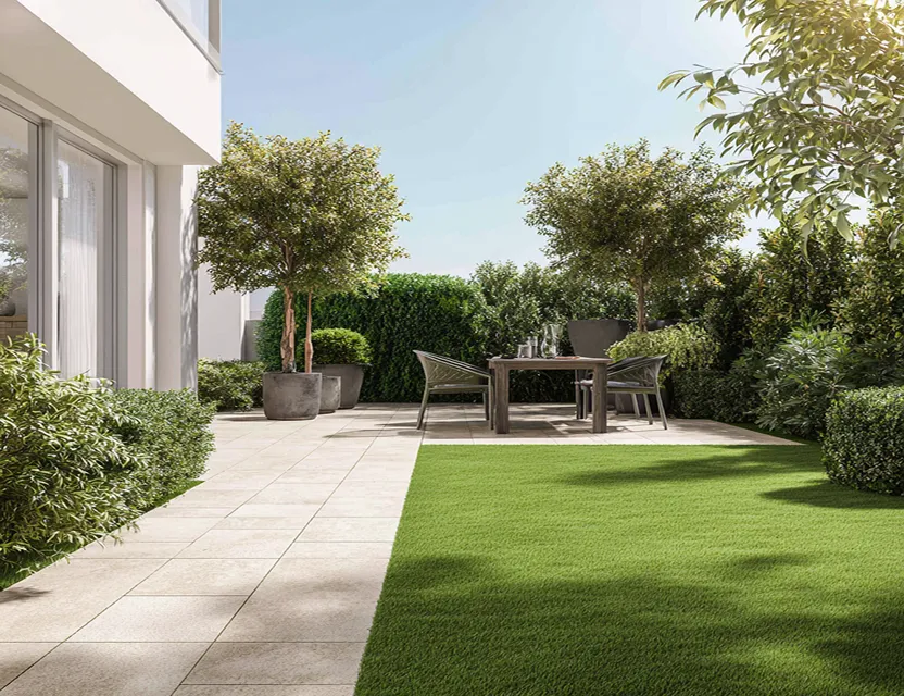 Terraza al aire libre con mesa y cuatro sillas rodeada de arbustos y árboles en macetas junto a un césped bien cuidado.