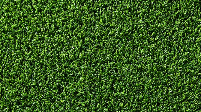 Mesa de madera clara con ocho sillas de mimbre gris en un área exterior con césped artificial.