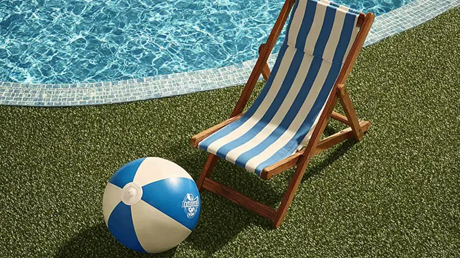 Silla de playa de madera con tela a rayas azules y blancas junto a una pelota de playa azul y blanca cerca de una piscina.