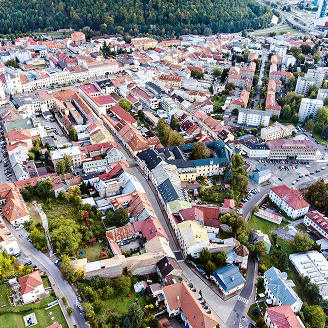 Bild Luftaufnahme einer Stadt mit Wohnhäusern, Straßen und Bäumen, umgeben von grünen Hügeln.