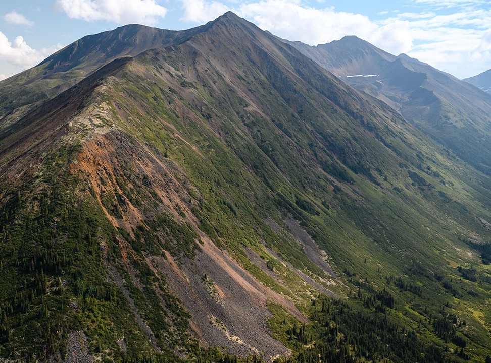 Wide view of a rugged mountain ridge covered with patches of green vegetation under a partly cloudy sky.