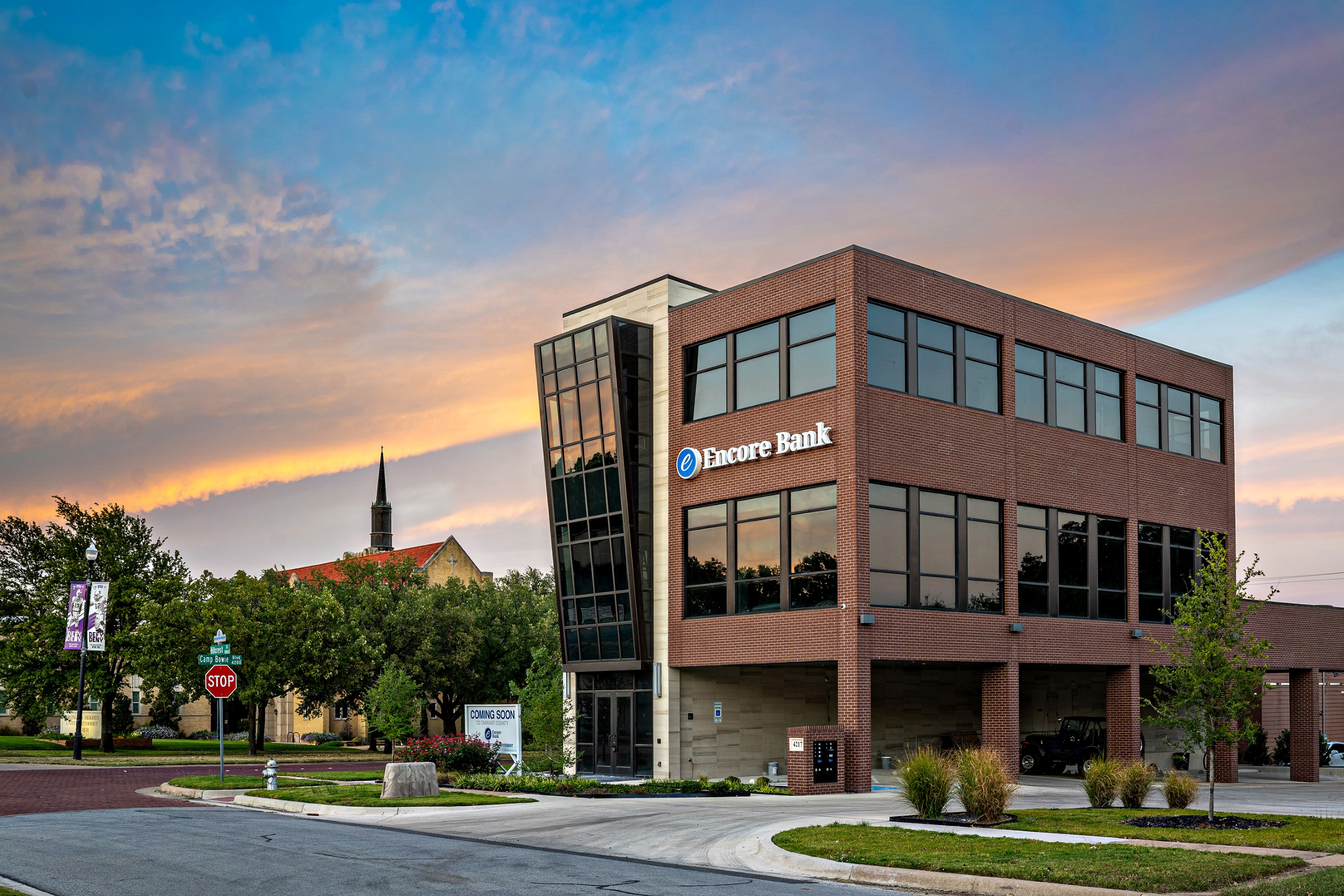 Modern three-story brick building with large windows and Encore Bank sign at sunset.