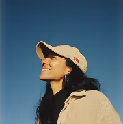 Smiling woman wearing a beige cap and jacket looking up against a clear blue sky.
