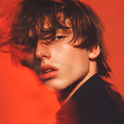 Close-up portrait of a young man with messy hair against a red background.