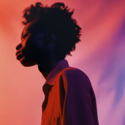 Side profile of a person with curly hair against a gradient background of red and purple hues.