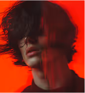 Person sitting on a stool reading a newspaper against a plain background.