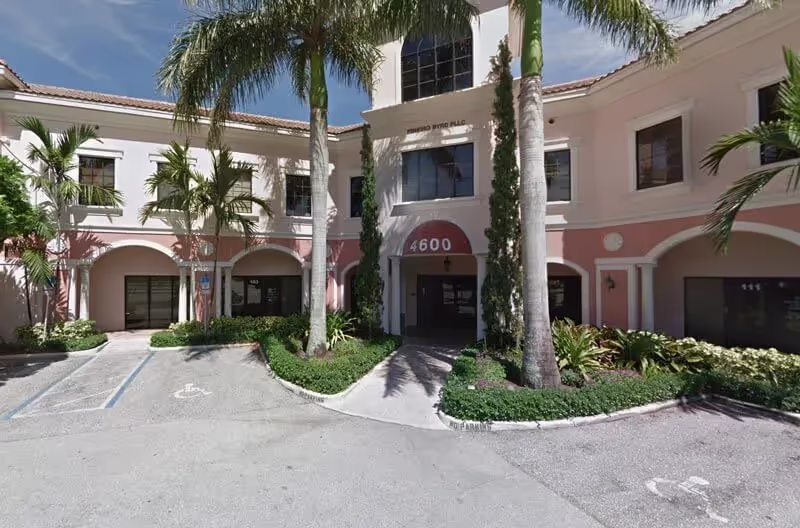 Front view of a pink-and-white office building with palm trees, labeled "4600", surrounded by gardens and a parking area.