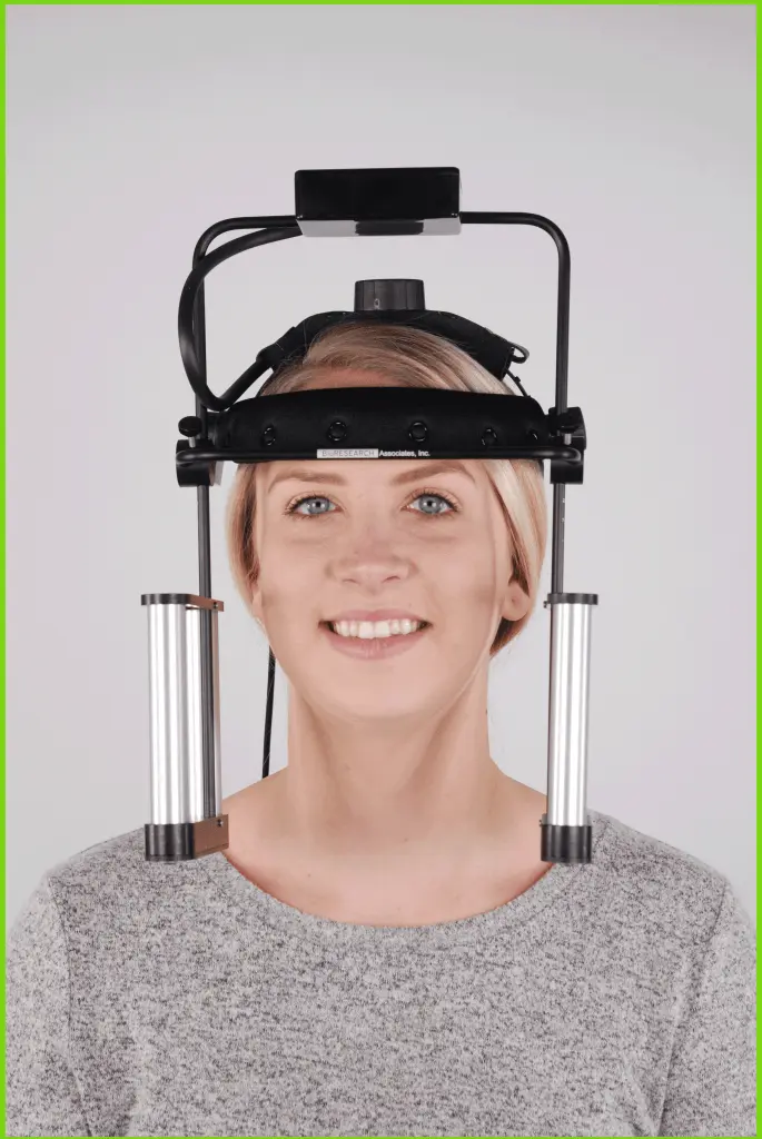 A woman wears a head-mounted device with metallic arms on either side, designed for a specialized procedure.
