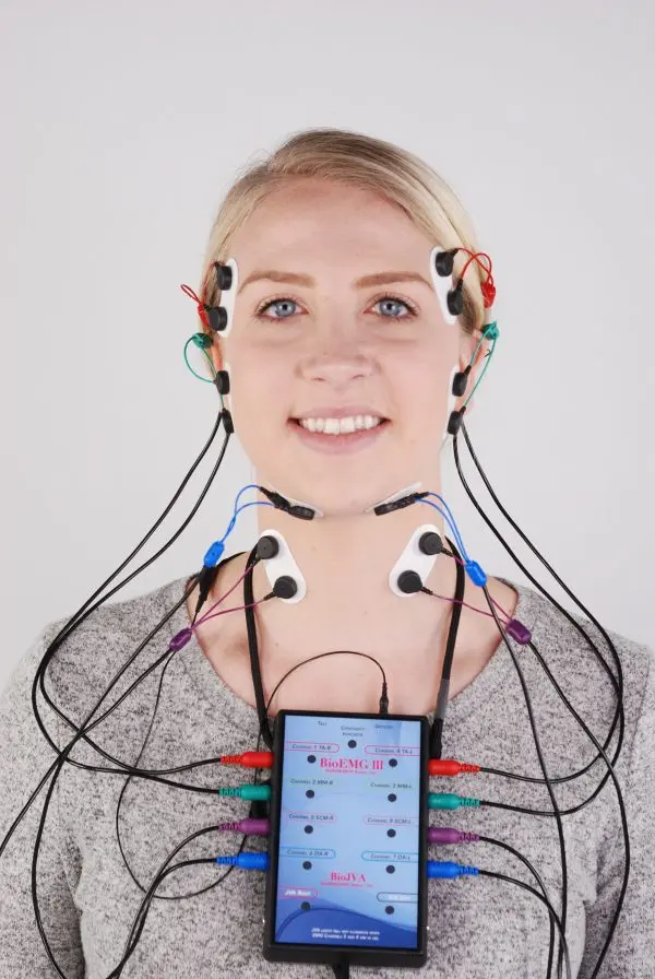 A person is connected to a diagnostic device with multiple wires and electrodes, displaying data on a screen.