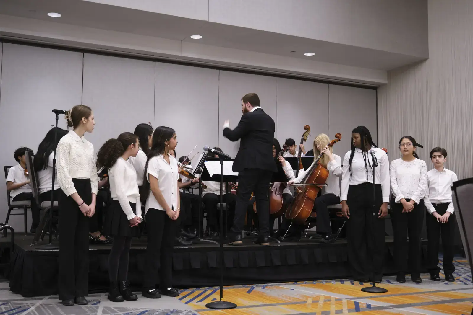 Students performing in orchestra with conductor during school music concert