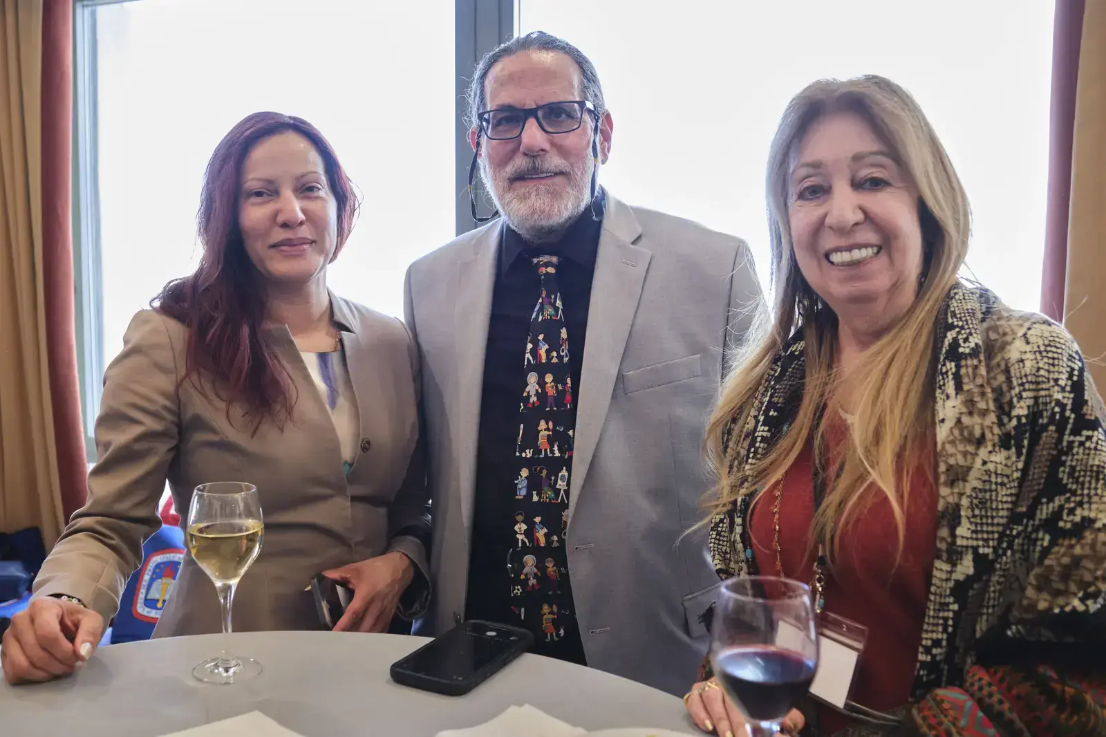 Three adults posing together at school event with beverages