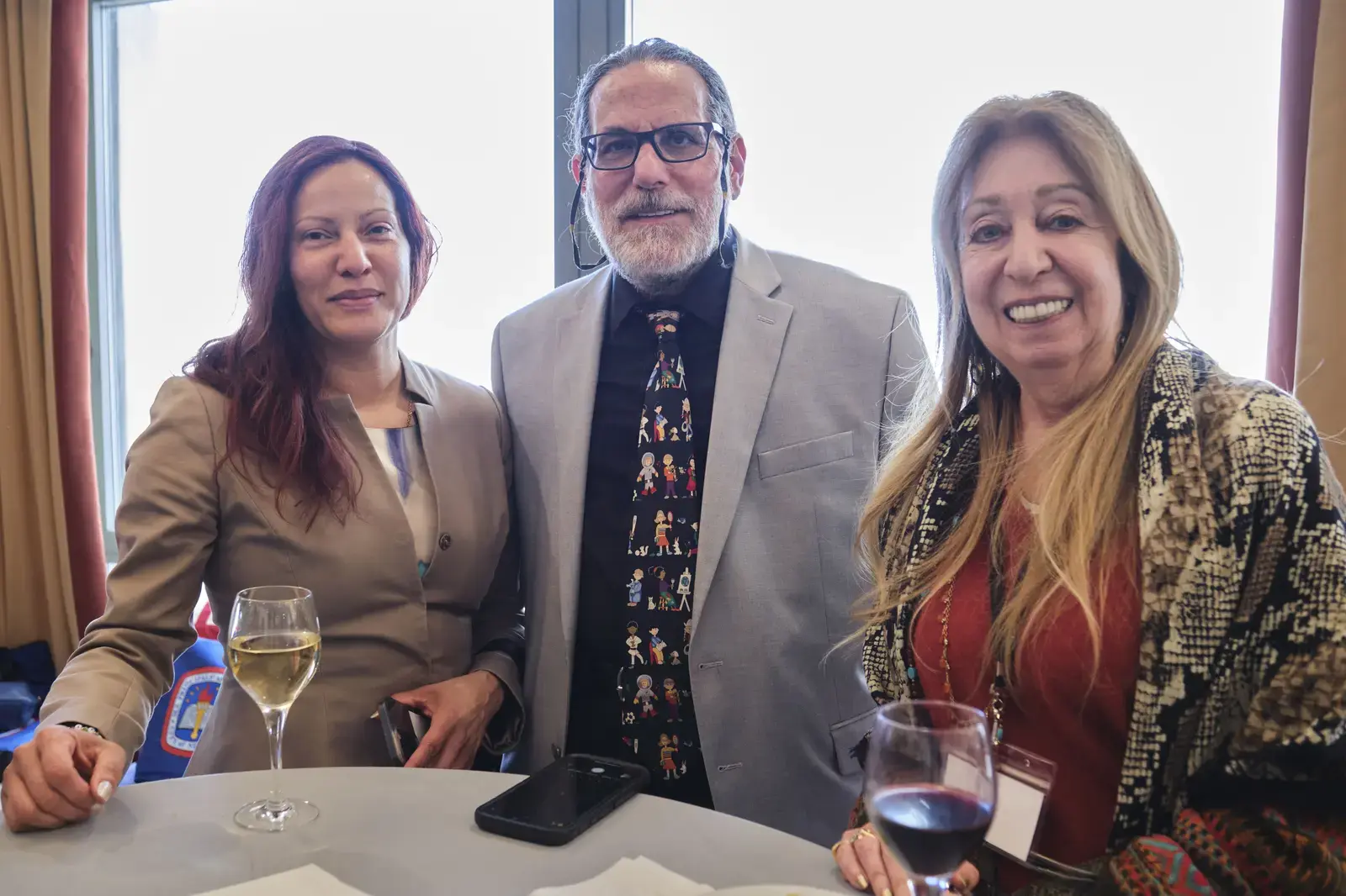 Three adults posing together at school event with beverages