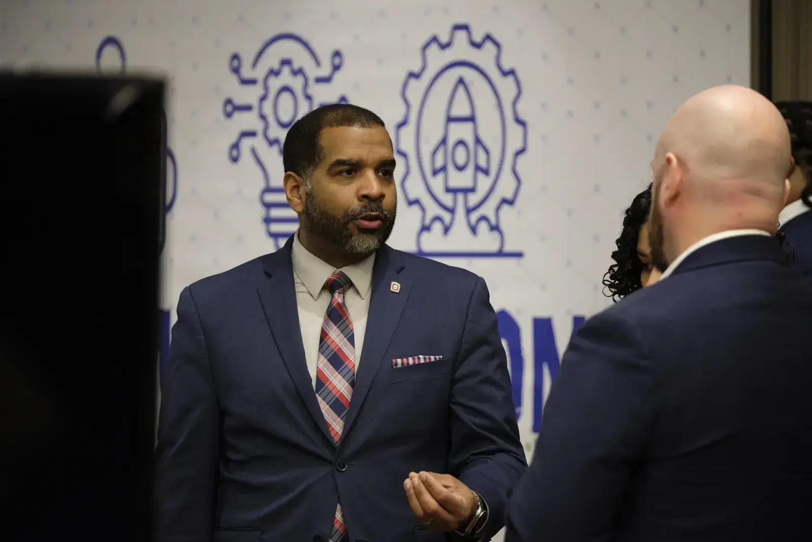 Professional in navy suit speaking with attendees at STEM event