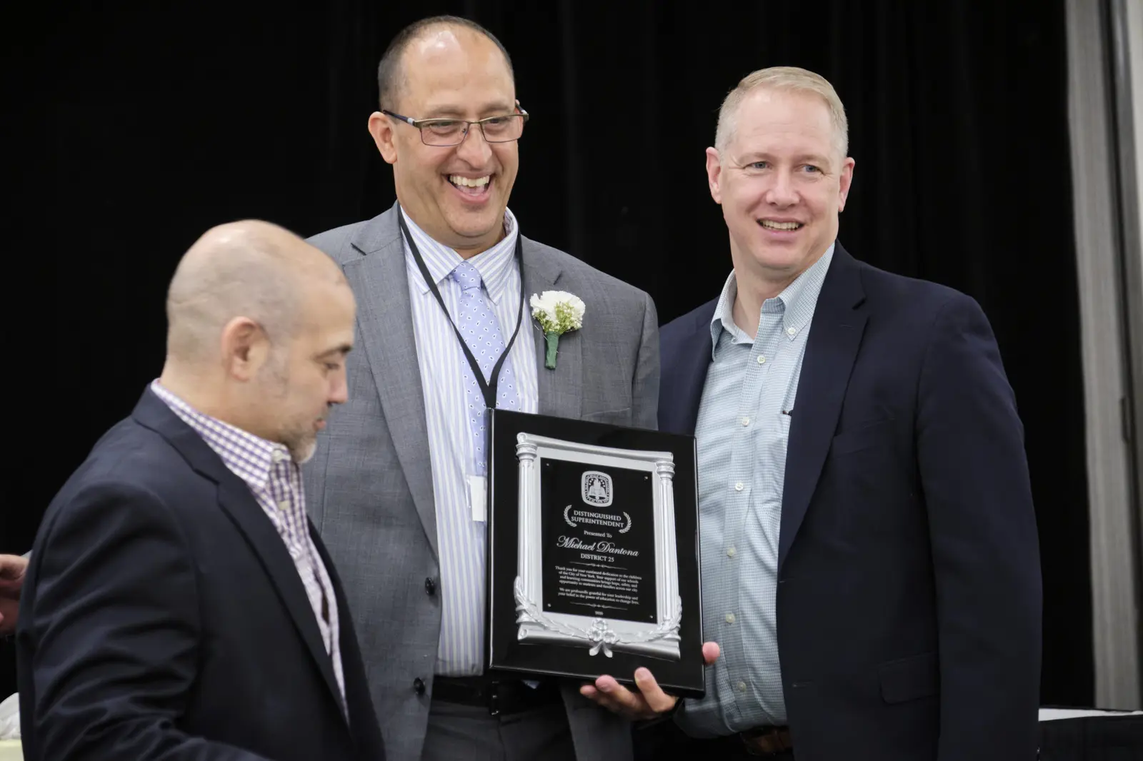 Three men at award ceremony, recipient holding framed plaque