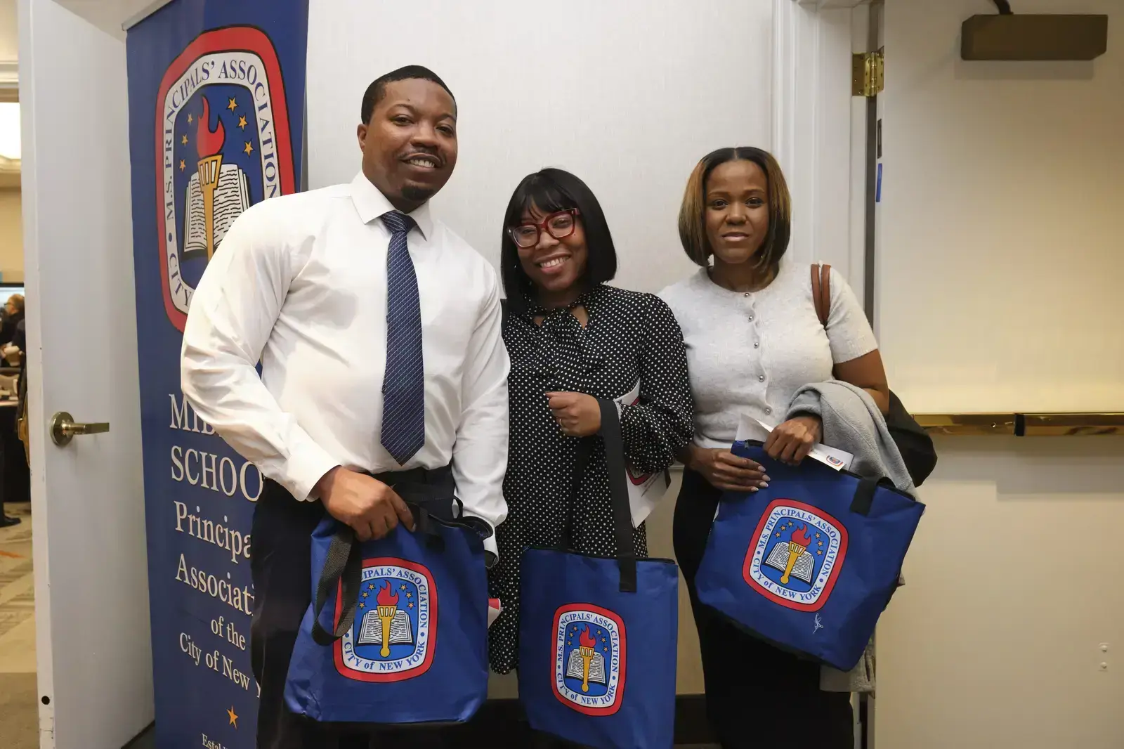 Three Principals' Association members holding blue tote bags at event