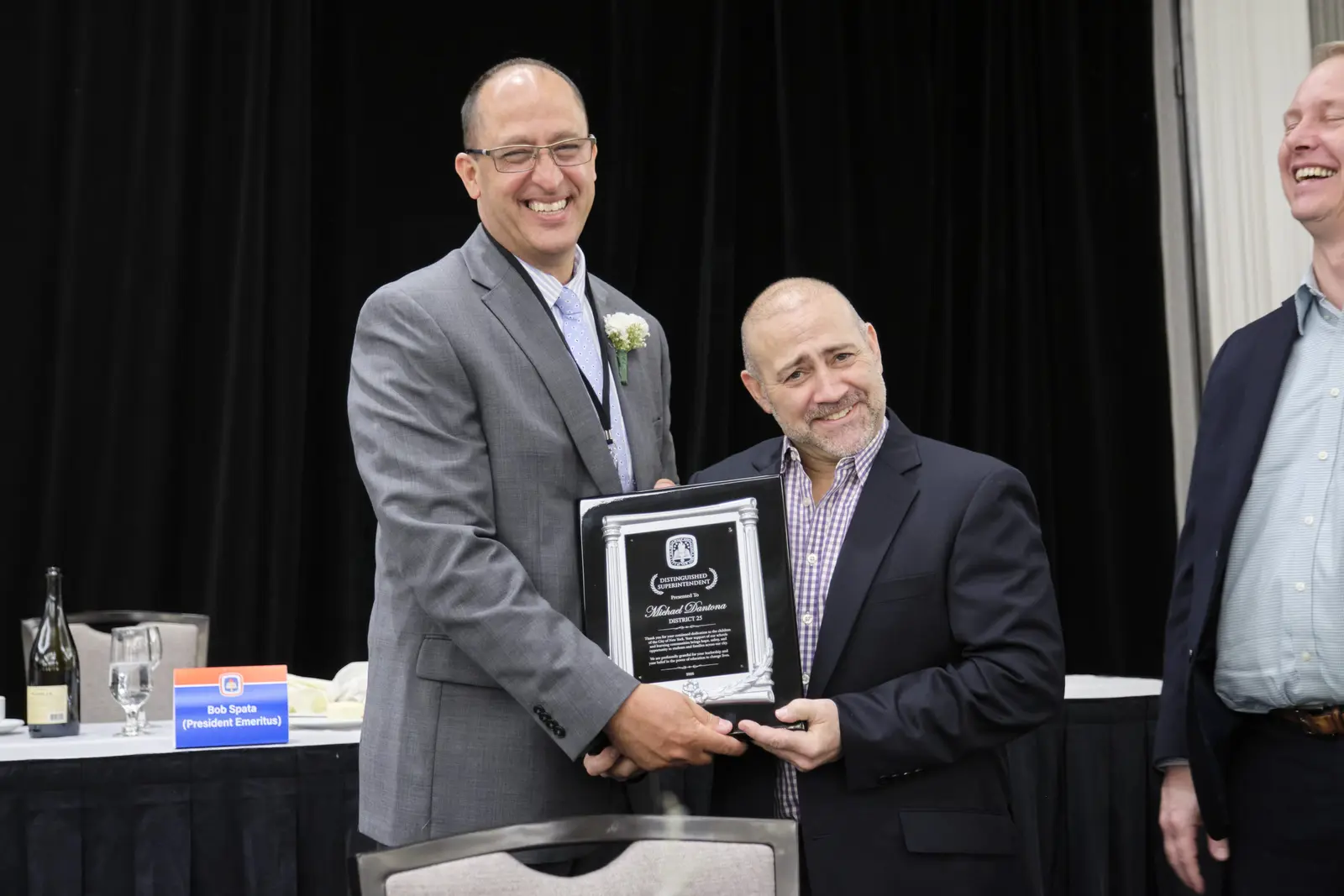 Two men smiling and holding recognition plaque at ceremony