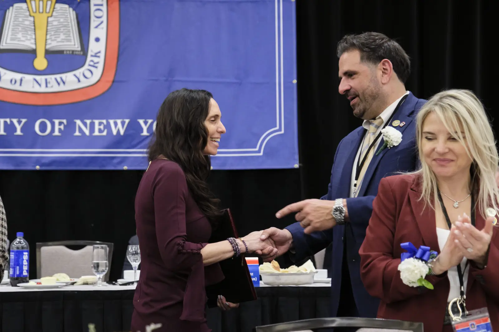 Woman in maroon suit receives award handshake at ceremony