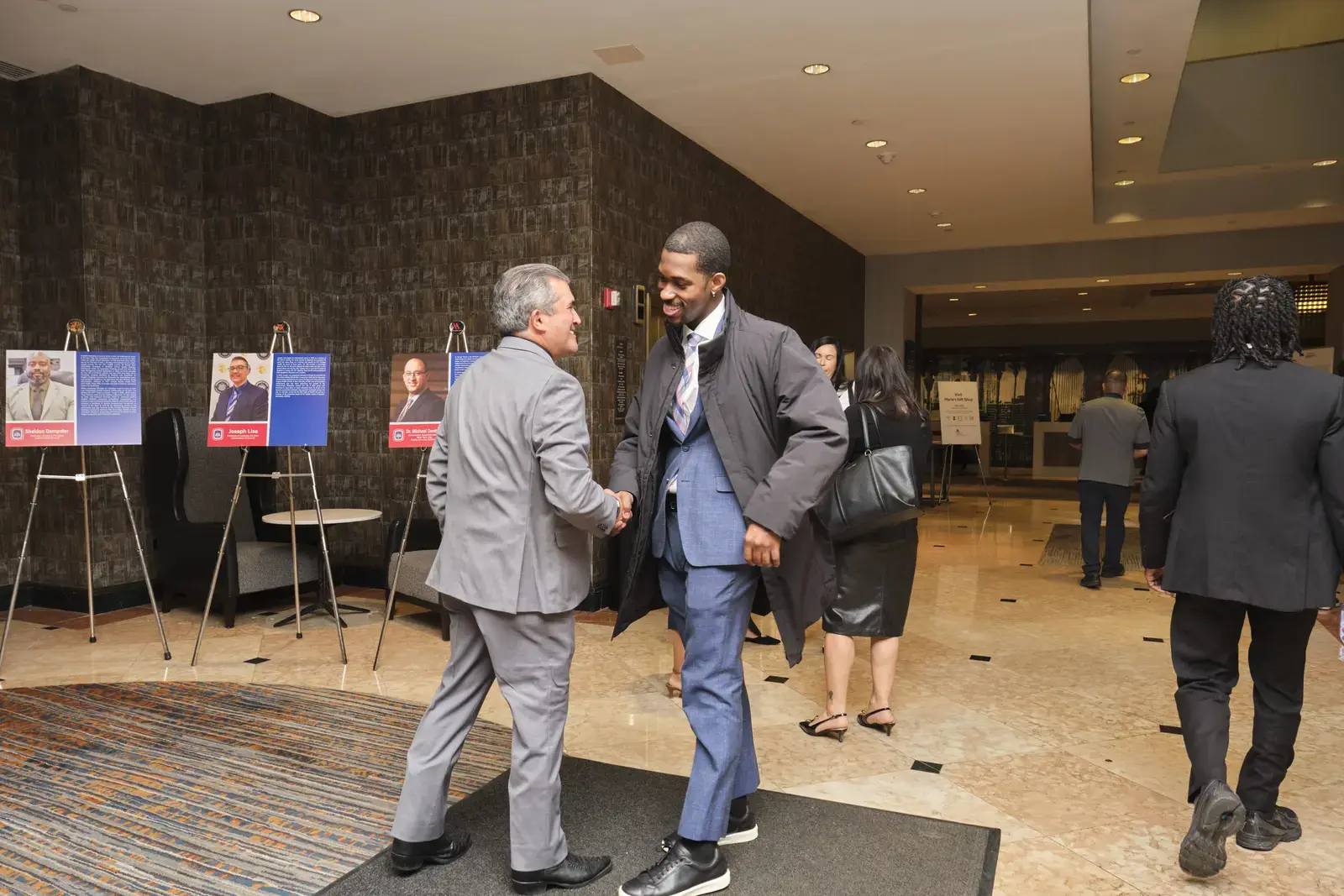 Two professionals shaking hands at networking event in lobby