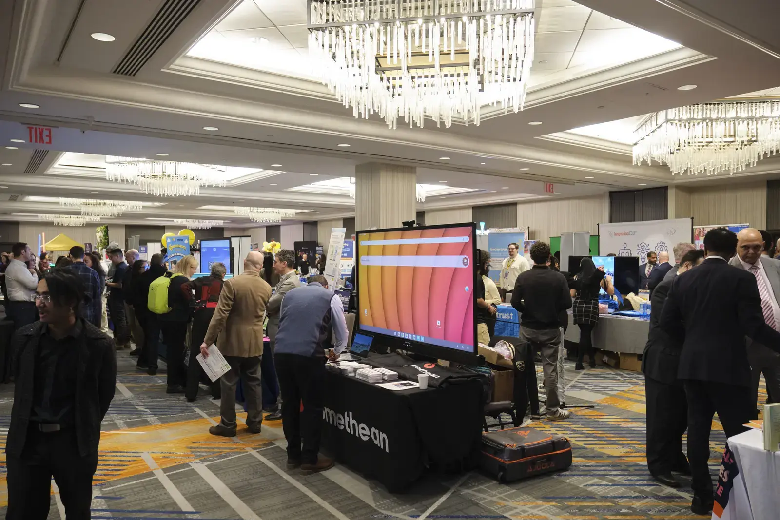 Attendees browsing exhibitor booths at school conference in hotel ballroom