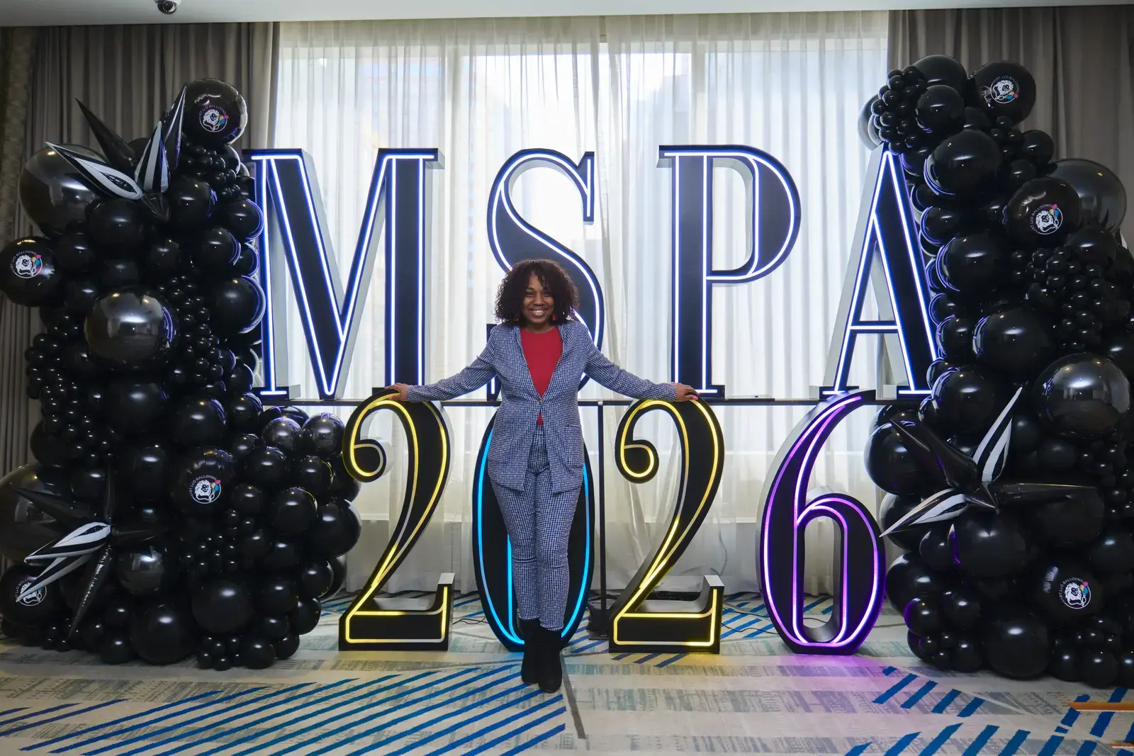 Woman celebrating at MSPA 2026 event with illuminated letters and black balloons