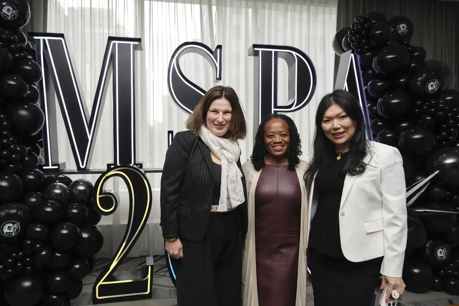 Three women posing at MSPA event with black balloon display
