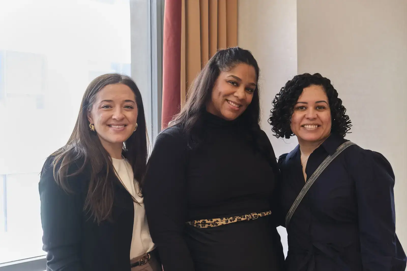 Three smiling women standing together in office setting