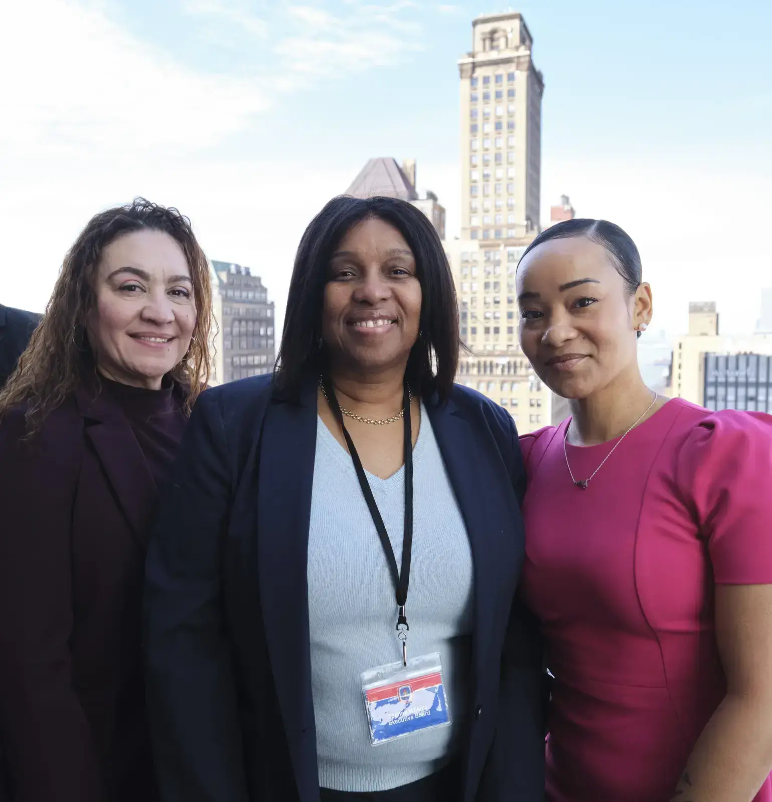Three professional women smiling together outdoors with city skyline