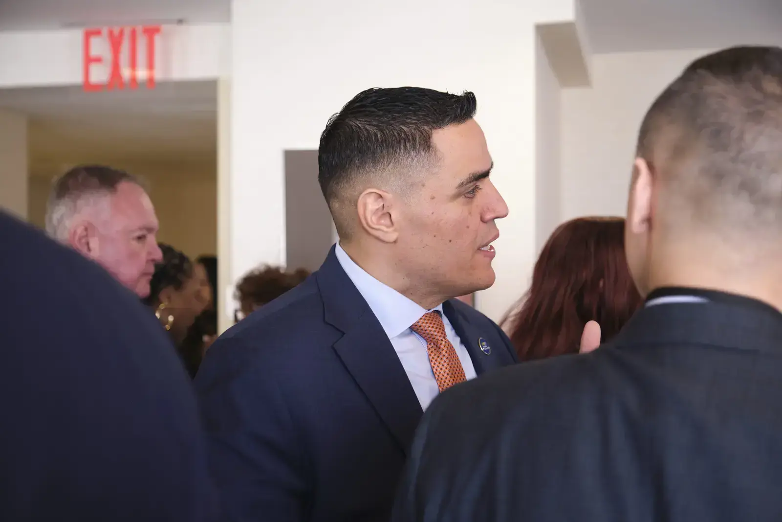 Man in navy suit speaking with attendees at school event