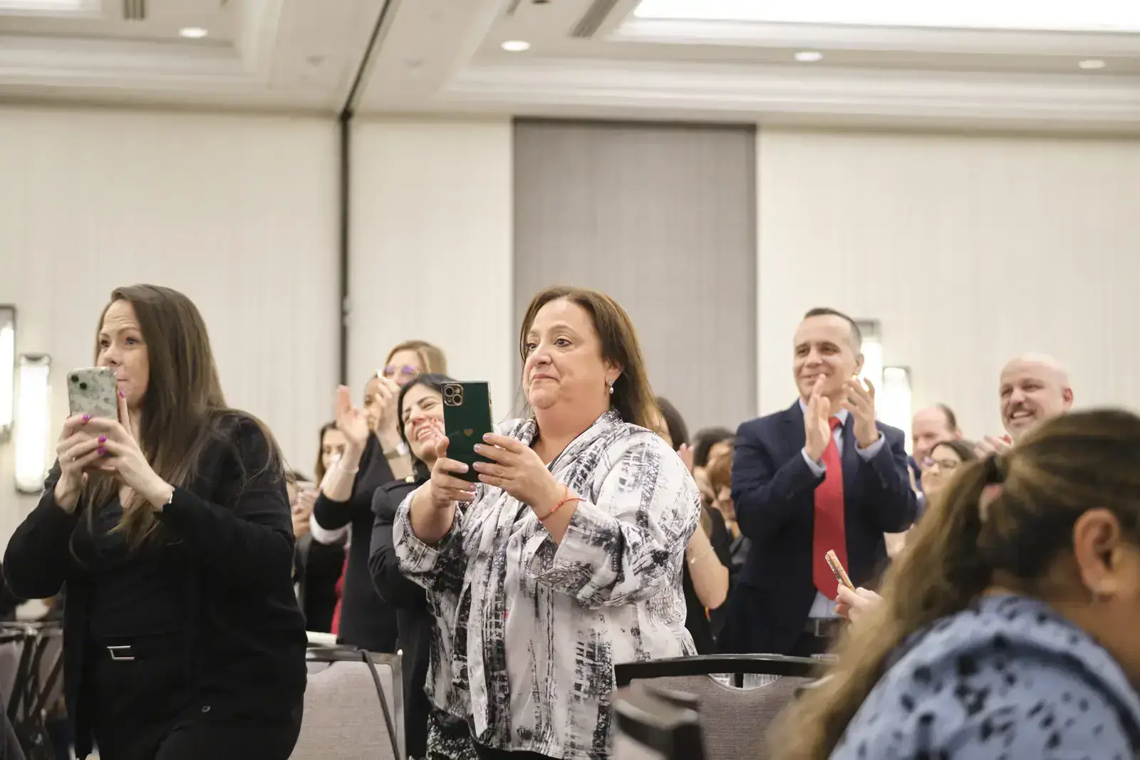Audience members applauding and recording with smartphones at event