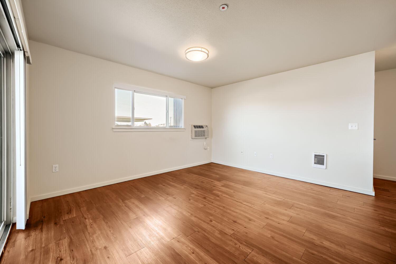 Spacious open living and dining area featuring wood-style flooring, natural light, and balcony access