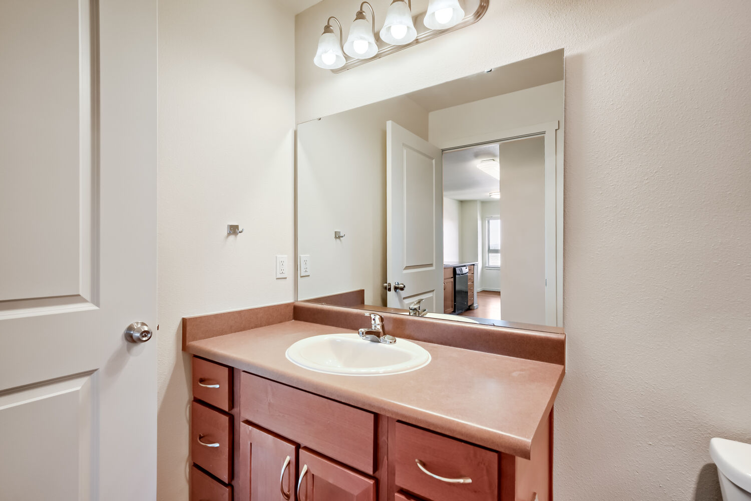 Modern apartment bathroom with single-sink vanity, wood cabinetry, oversized mirror, and bright vanity lighting