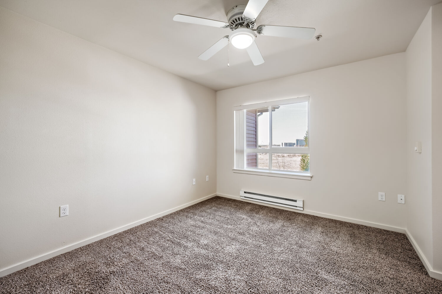 Spacious carpeted bedroom with ceiling fan, large window, and abundant natural light