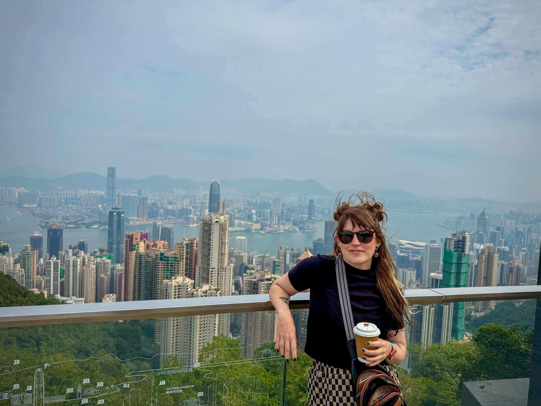 A woman leaning on a railing high above a the city of Hong Kong behind her