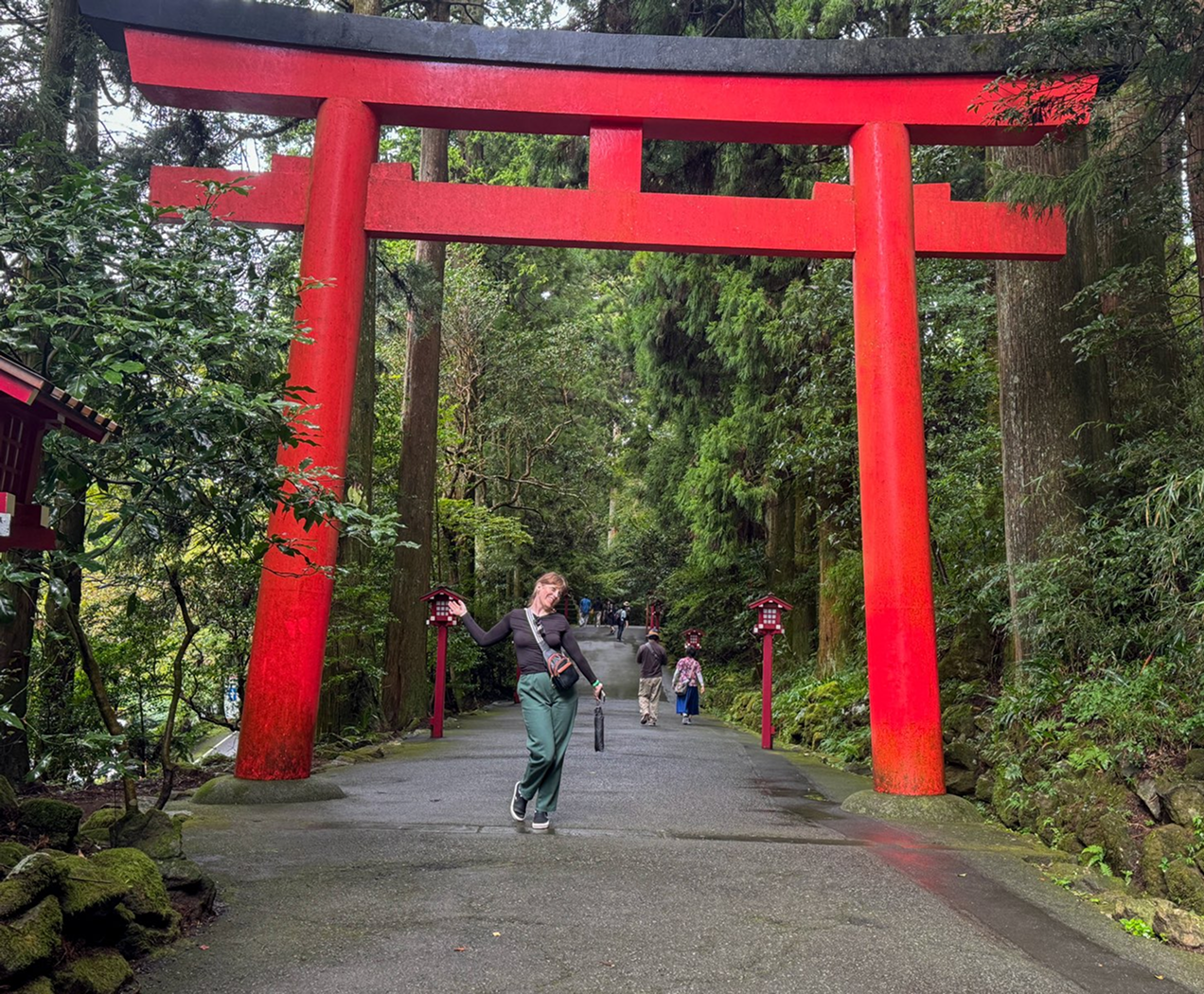 a woman standing in front of a large red Japanese shrine comprised of two poles on either side of the walkway and joined together by perpendicular pieces to make a decorative top