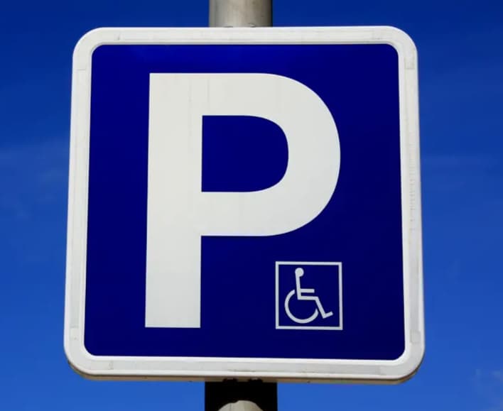 Blue parking sign with a white letter P and a wheelchair symbol indicating accessible parking.